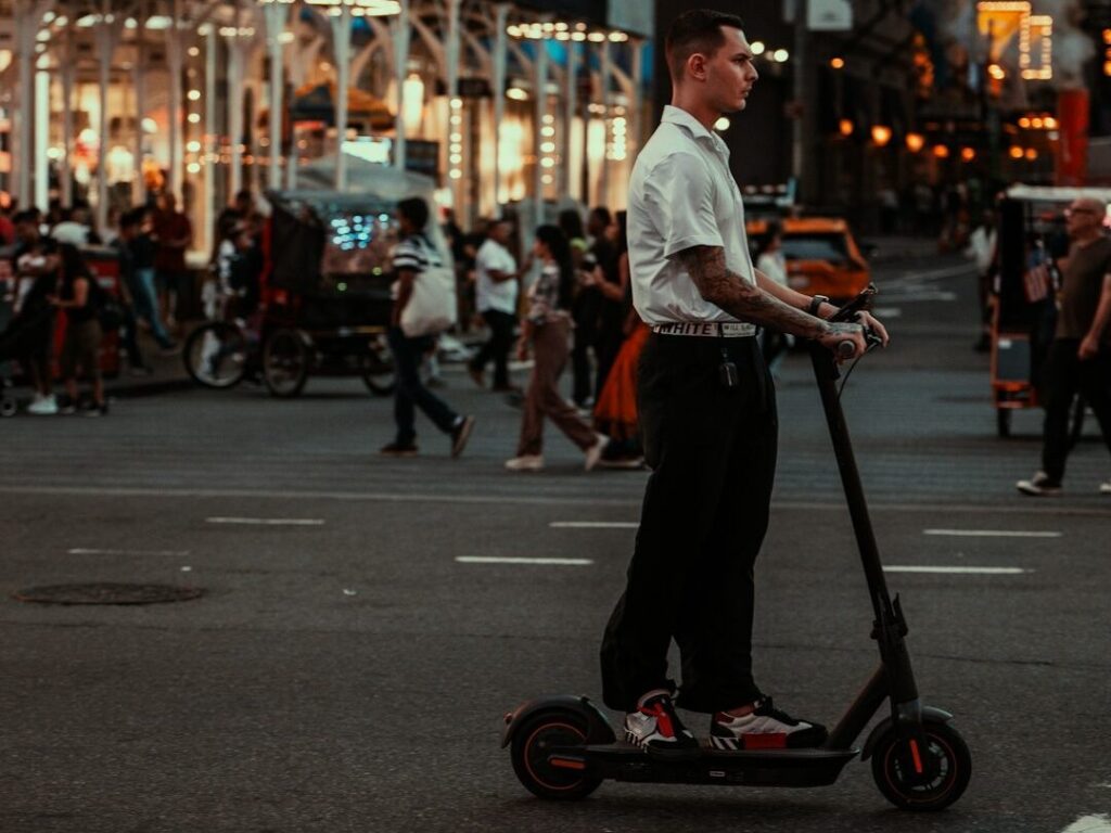 Man riding an electric scooter through a busy city street, demonstrating the importance of following electric scooter rules, including escooter speed limits and helmet requirements for safe urban travel.